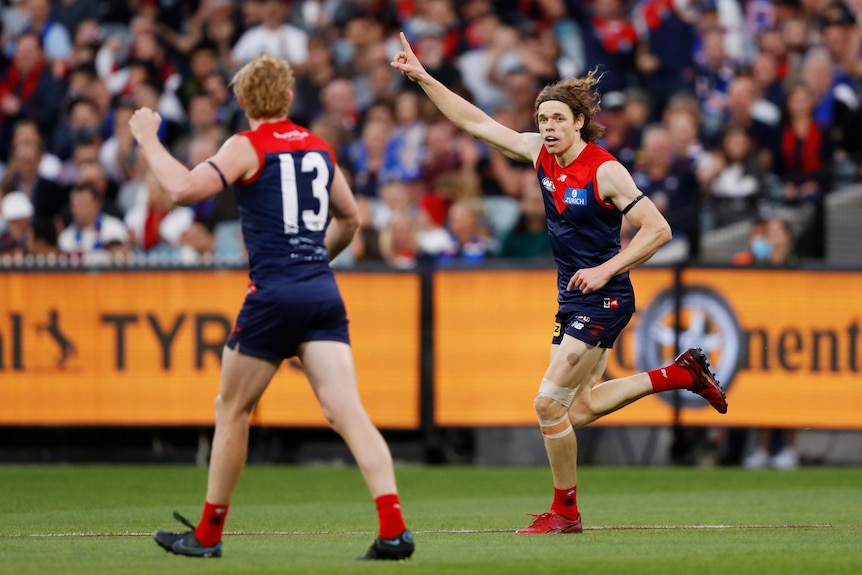 An AFL forward points to the sky in triumph as he runs towards a teammate after kicking a goal.