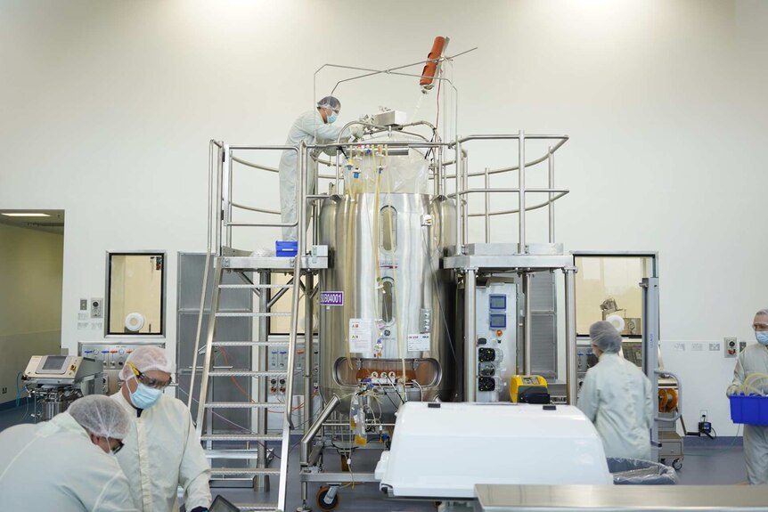 People in white lab coats and hairnets in a room with stainless steel laboratory equipment