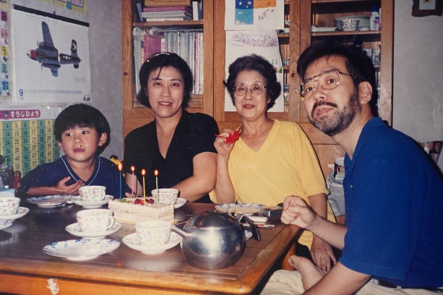 An old photograph of the Miyazawa family in a living room surrounding a birthday cake