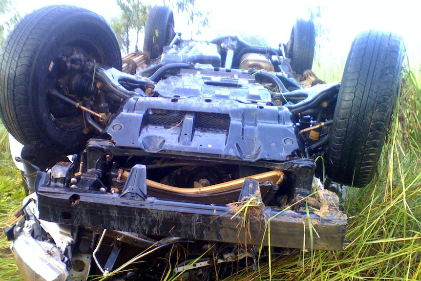 A four-wheel drive lying on its roof in long grass.