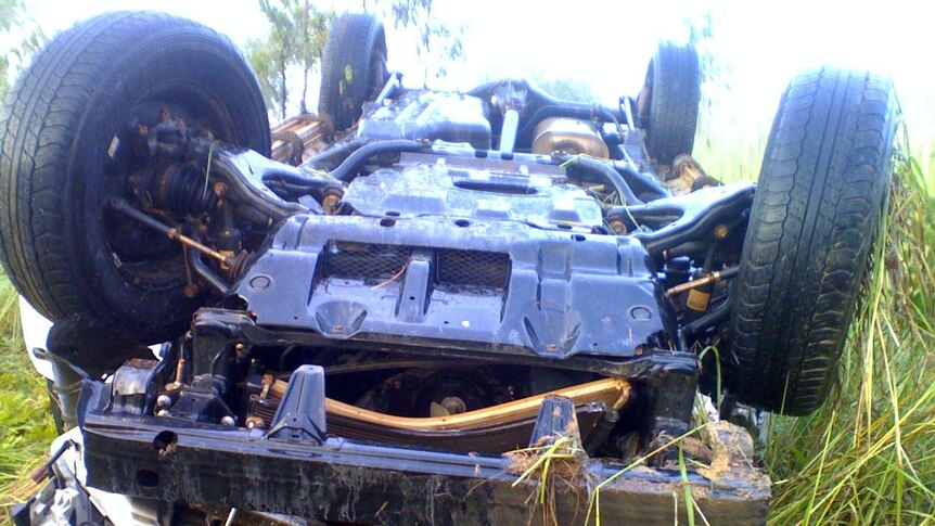 A four-wheel drive lying on its roof in long grass.