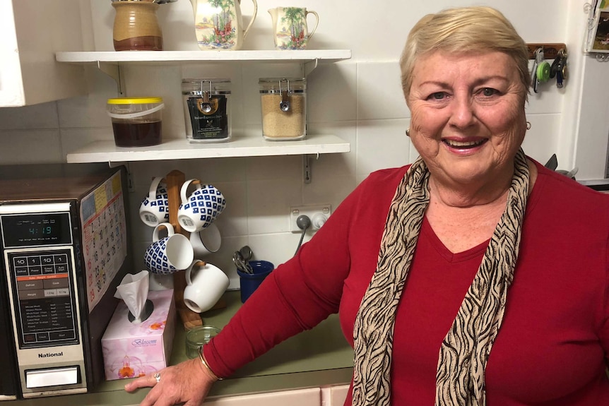 A woman in a red top and black striped scarf stands in a kitchen next to a microwave.