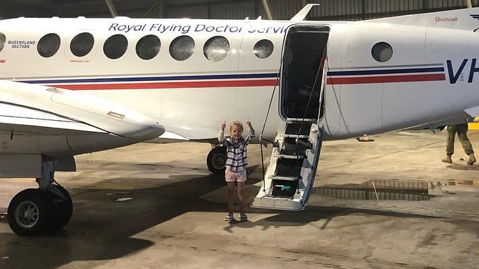 A young girl stands in a aircraft hanger in front of an RFDS plane