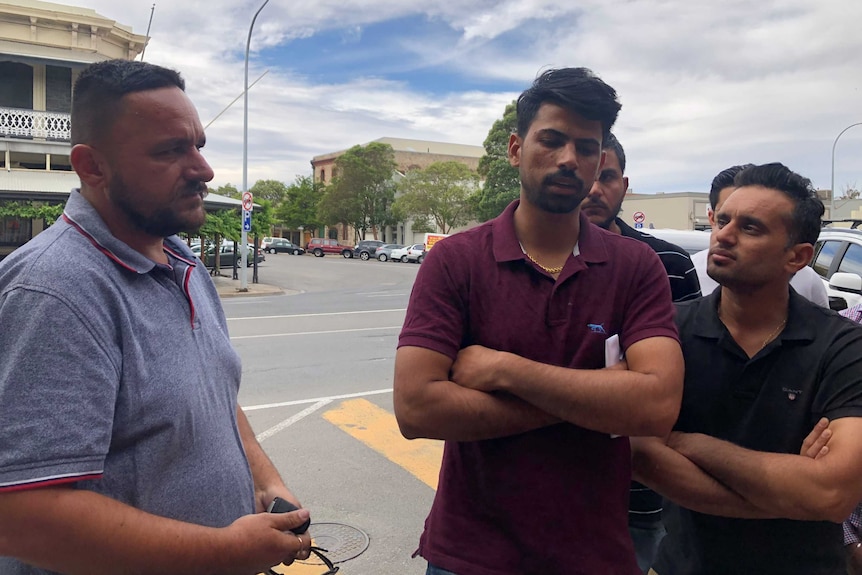 A group of men stand by the road and speak with the media