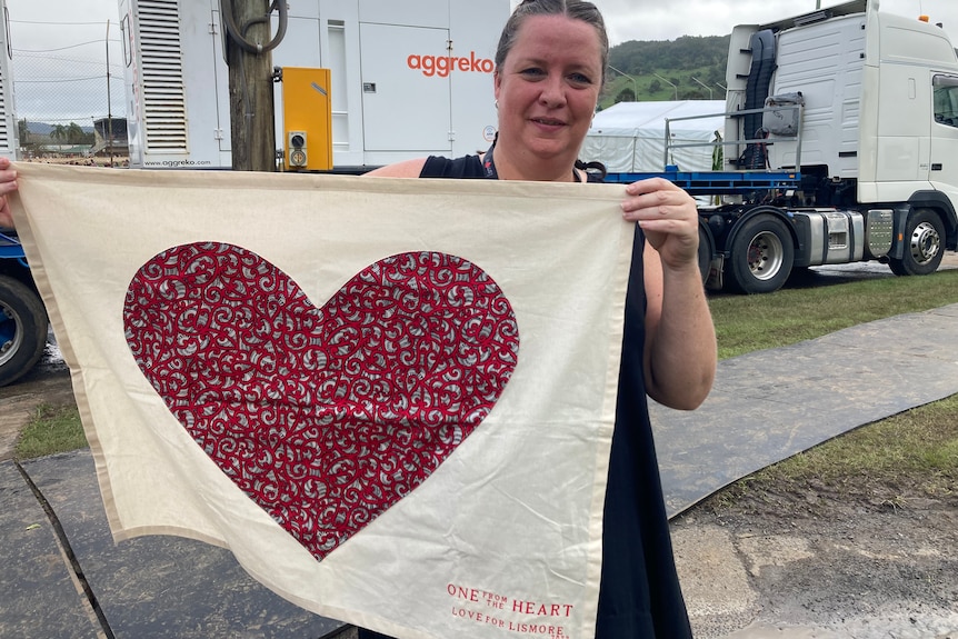 A woman holding up a banner with a red heart on a plain background.