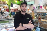 A young man stands in a store with sweets behind him, he is in a black uniform.