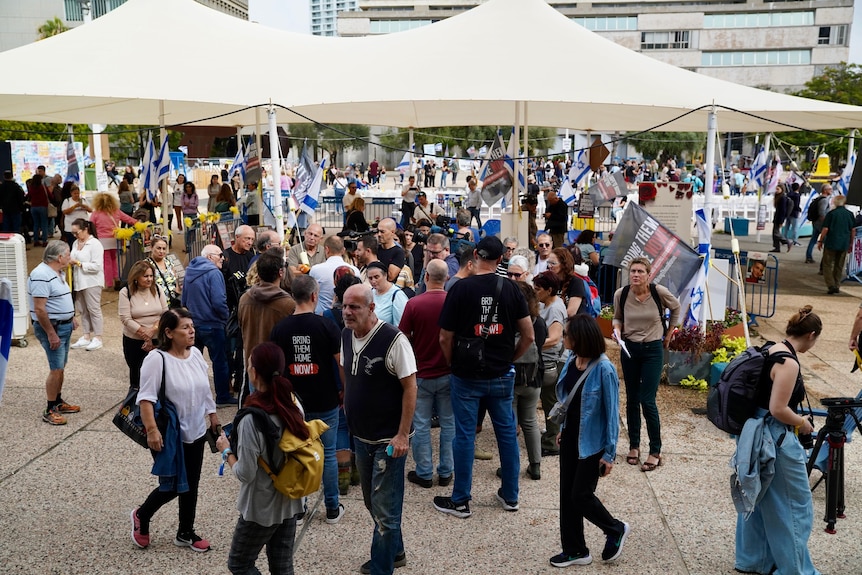 A wide shot shows a busy square with posters and yellow ribbons