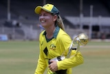 Australian cricketer Meg Lanning smiles as she cradles the tri-series trophy under her arm.