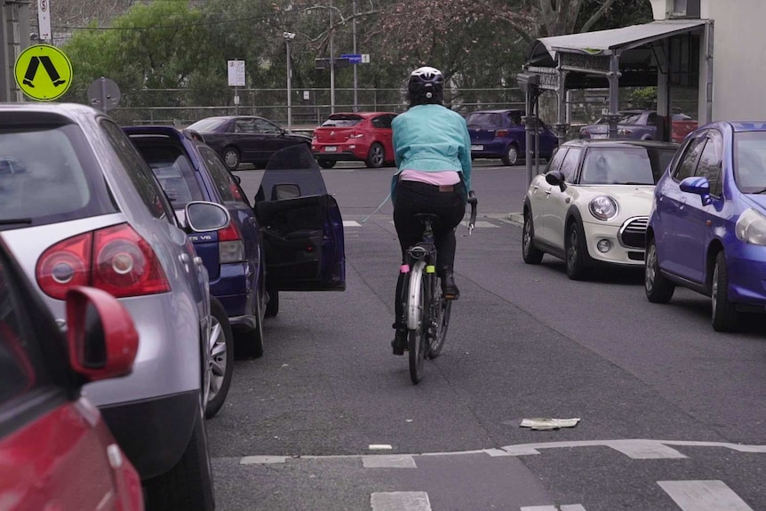 A door is being opened by a car infront of Julia on her bike, she is verring towards the right to avoid the door.