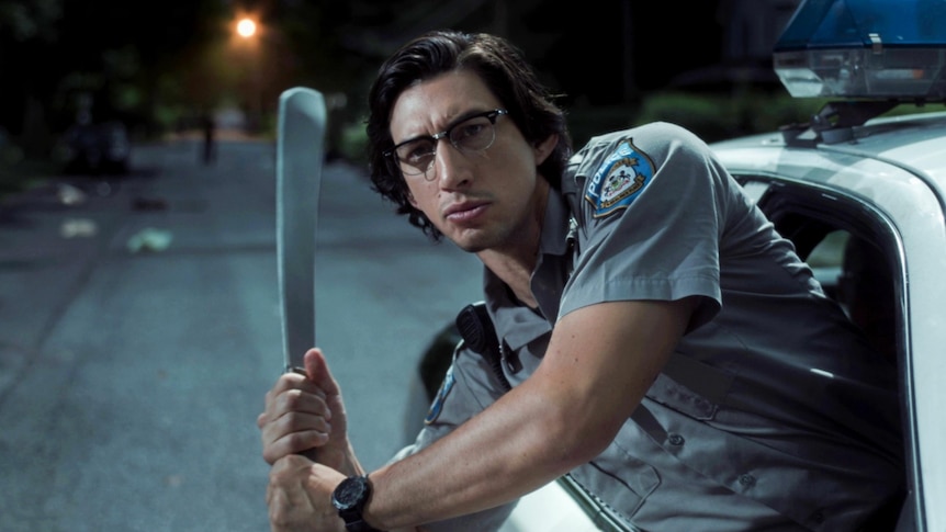 A police officer holds a large knife in a batting position and leans with upper body out of police car window at night time.