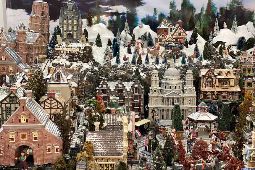 Miniature Christmas village with snow topped mountains and pine trees in the background.