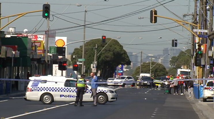 A commercial strip with police tape across the road and a police car parked on the centre line.