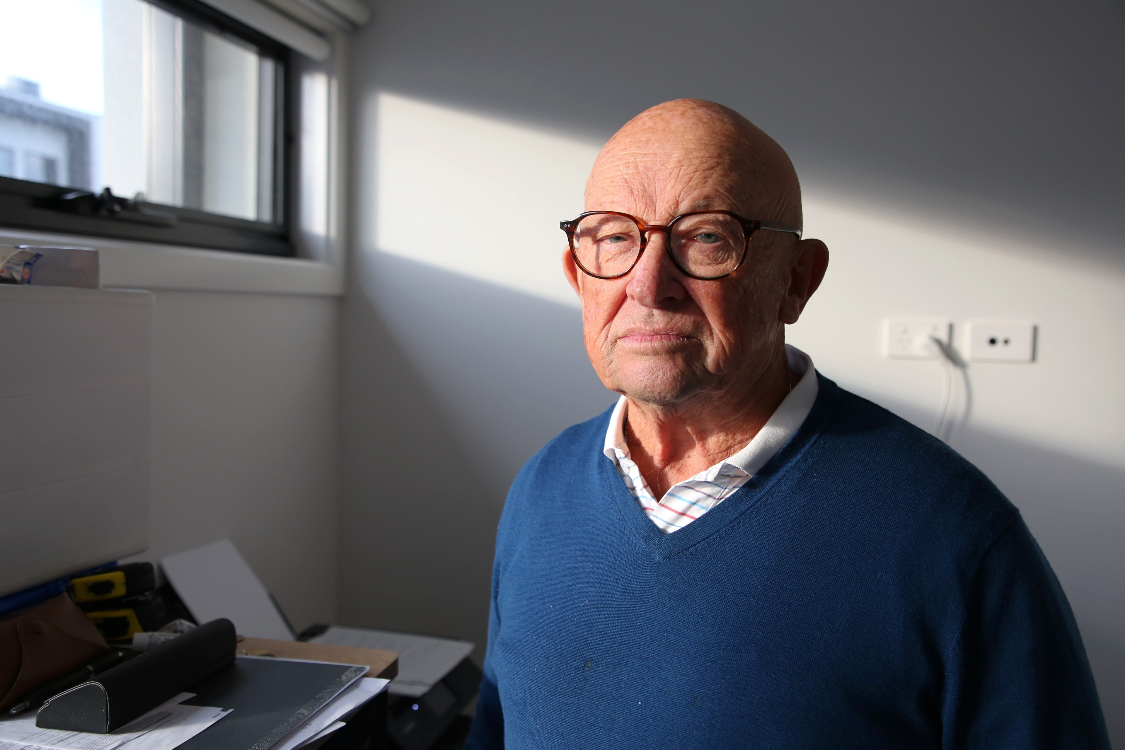 Light shines through a window onto a man wearing a blue jumper and glasses.