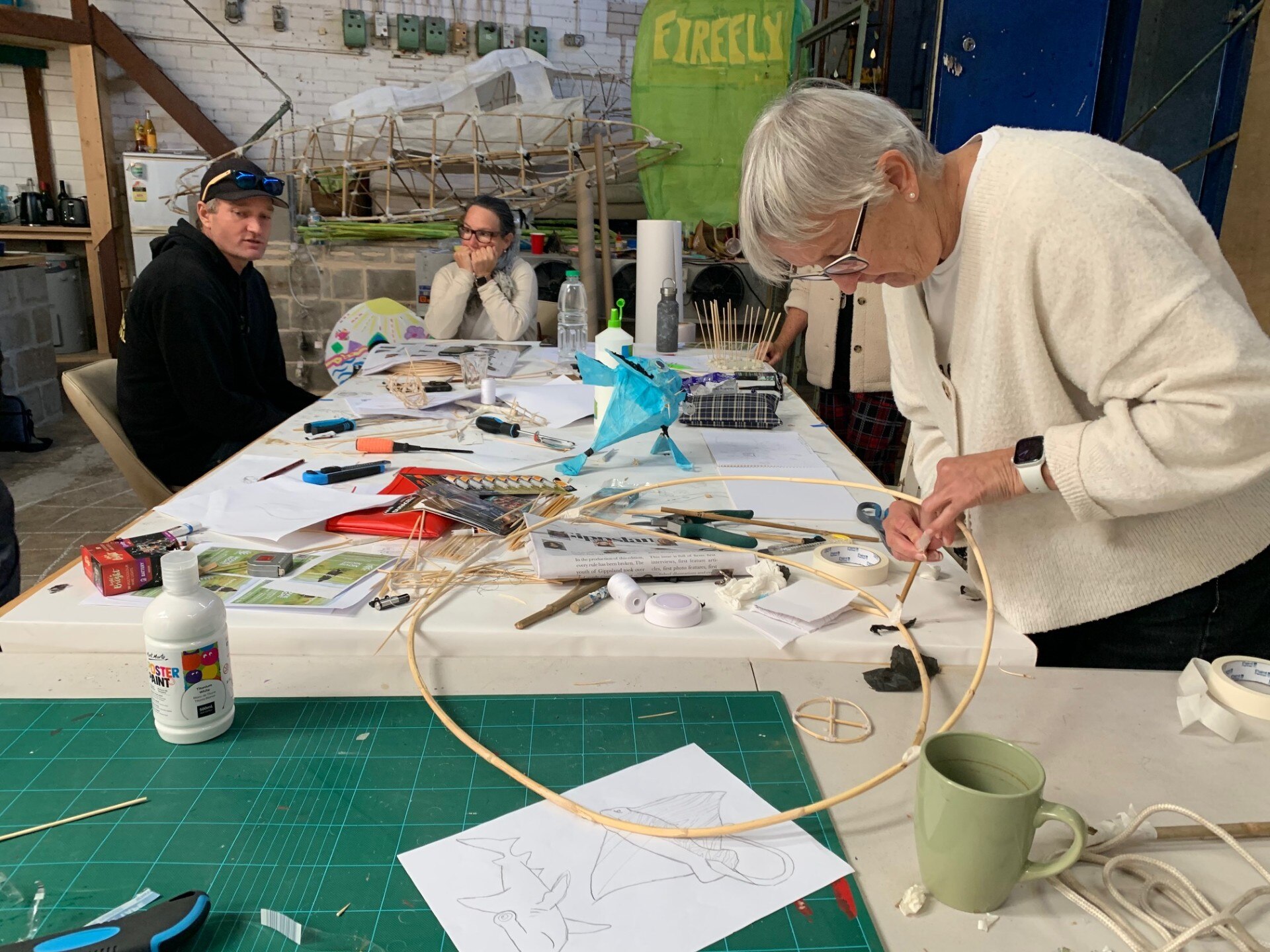 A woman bends over a large, crafty table as she works on a circular object.