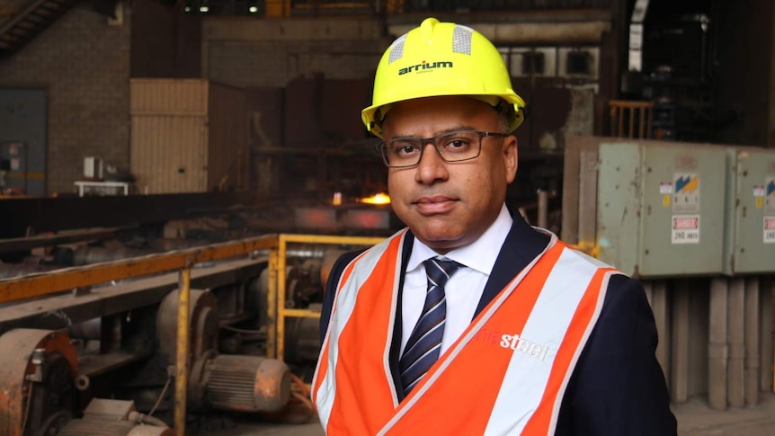Sanjeev Gupta in a hard hat with a steelworks production line behind him.