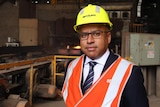 Sanjeev Gupta in a hard hat with a steelworks production line behind him.