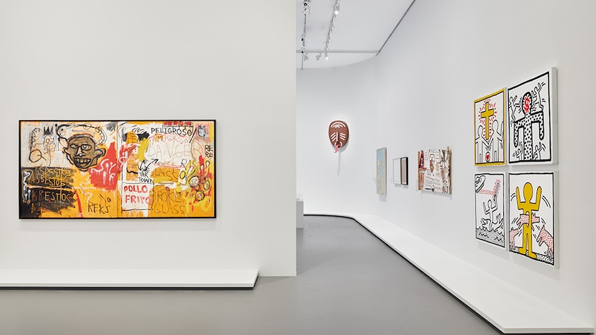White gallery space displaying frenetic red, orange and yellow painting on left wall and various smaller artworks on right wall.