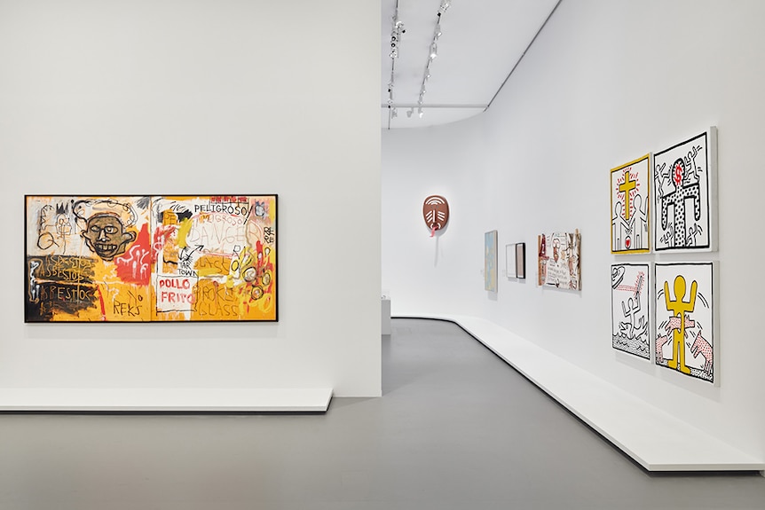 White gallery space displaying frenetic red, orange and yellow painting on left wall and various smaller artworks on right wall.