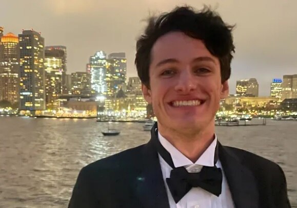 An image of a young man smiling into a camera while wearing a tuxedo.