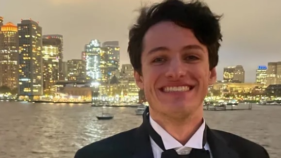 An image of a young man smiling into a camera while wearing a tuxedo.