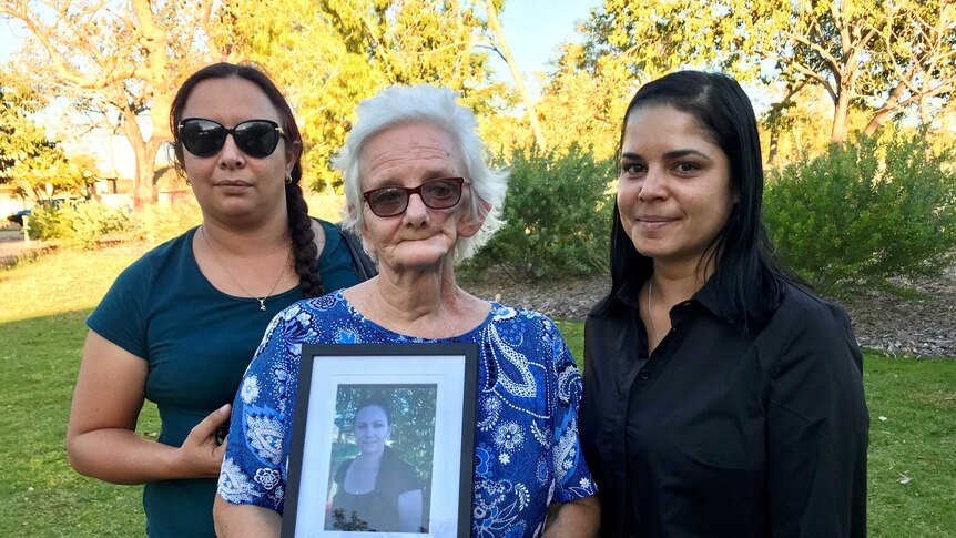 Three women stand on the lawn of Broome Courthouse holding a photo of a loved one who died in a car accident.