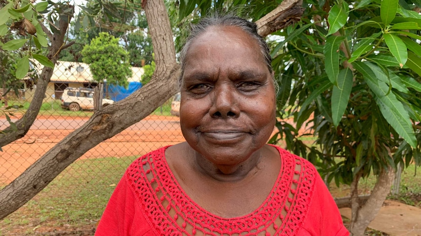 Jeannie Gadambua, stands, wearing a red dress in Maningrida.