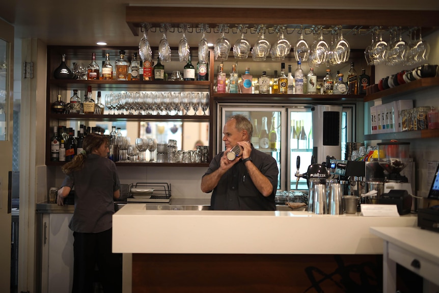 A man working behind a bar shakes a cocktail.