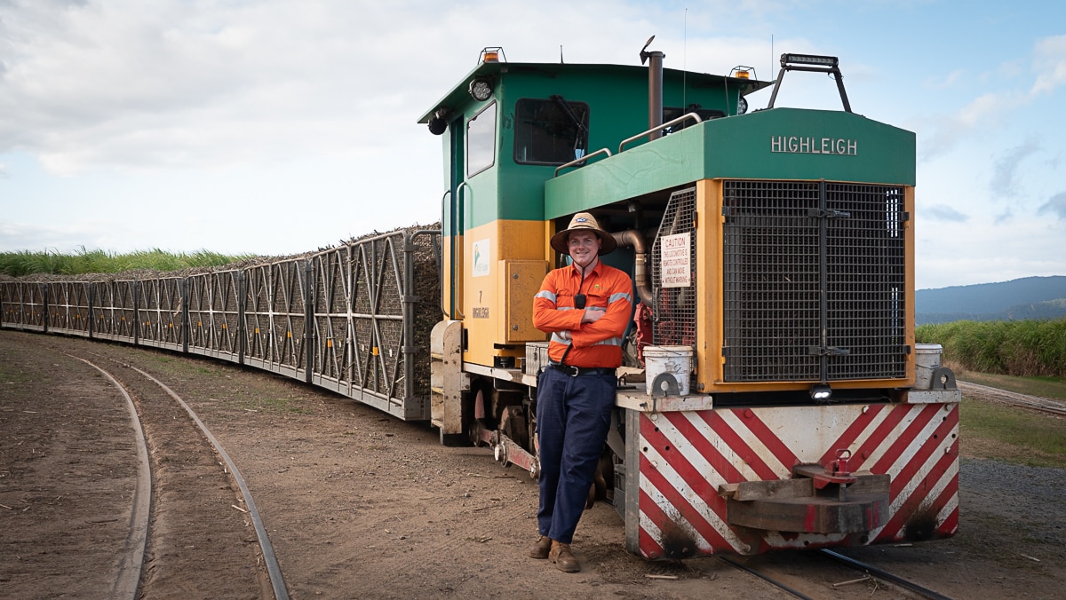 man leans on cane train with load of sugar cane in background