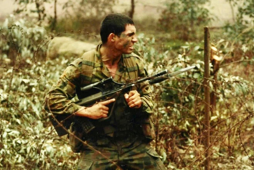 A man in military camouflage holding a rifle, appearing to be running.