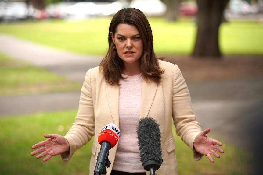 A woman wearing a beige blazer – Sarah Hanson-Young – speaking into two microphones.