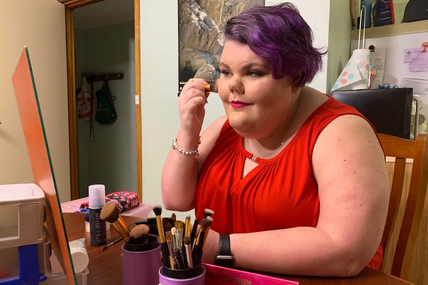 A teenage girl applies make-up in front of a mirror.