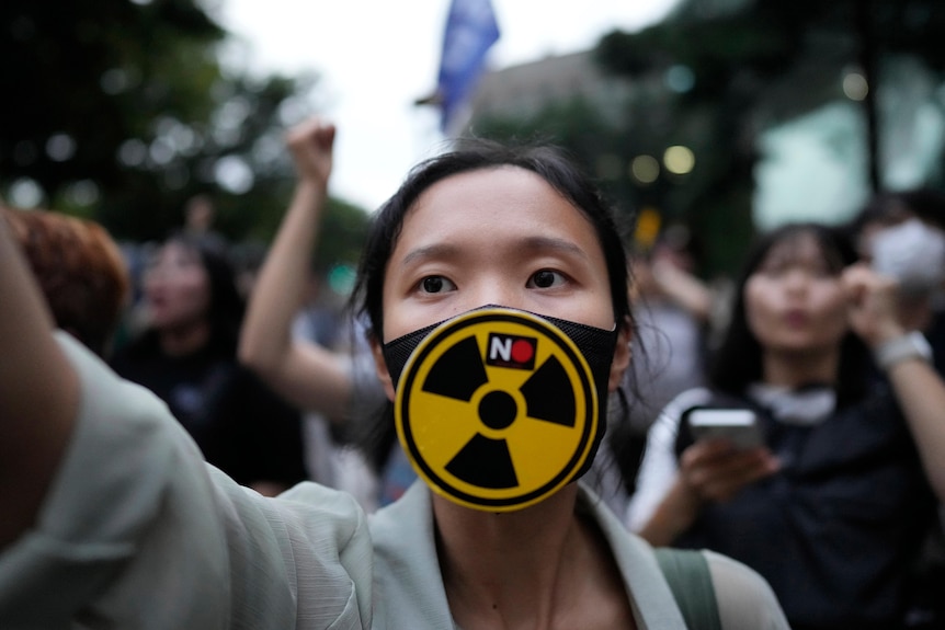 A South Korean woman wearing a face mask with radioactive symbol and the words 'no' during protest.