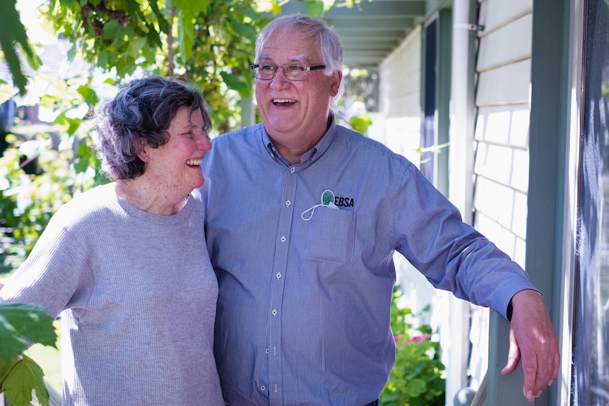 A photo of an older couple smiling and laughing with greenery around them.