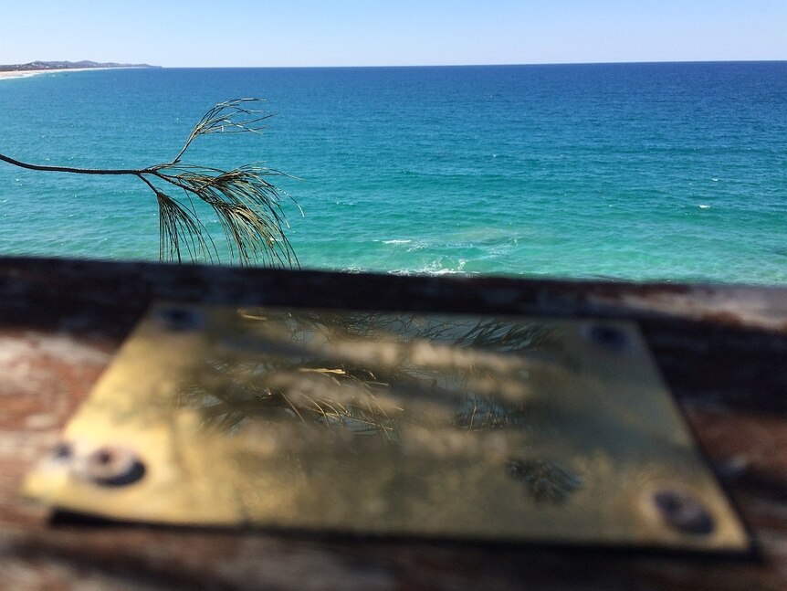 A plaque on a wooden barricade overlooking the ocean.
