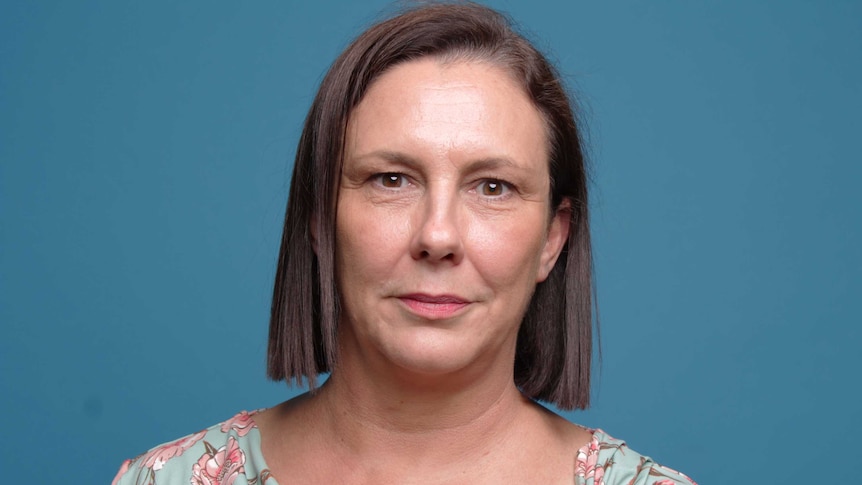 Woman with floral top and neutral expression, before a blue background.