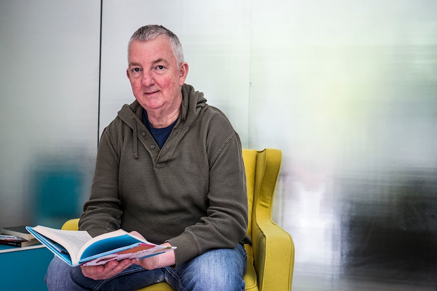 Duncan McNab sits in an armchair, holding a book.