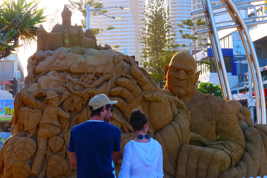Two people stand in front of a large sculpture of a rock-like figure.