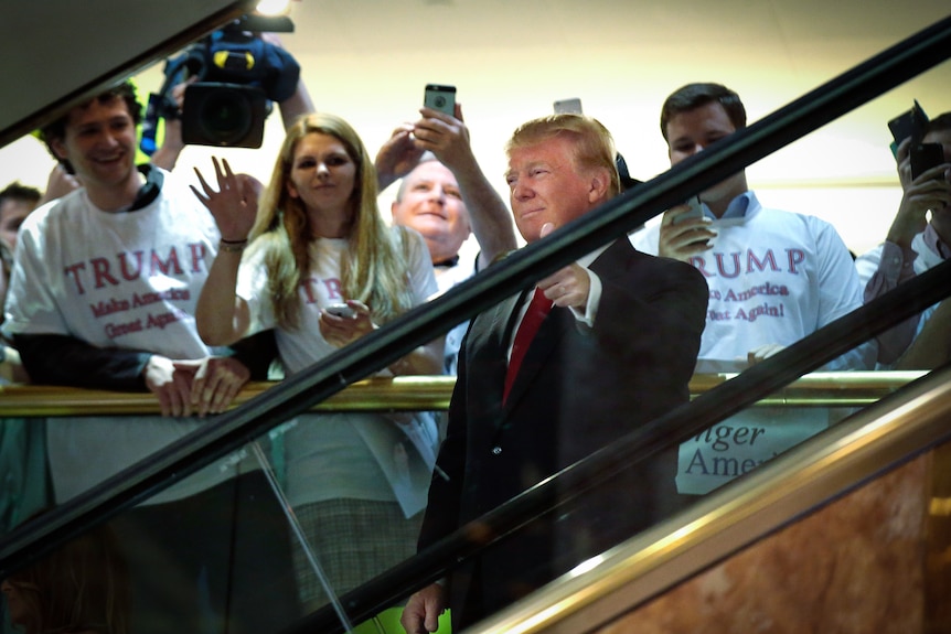 Donald Trump smiles and gives the thumbs up while riding an escalator 
