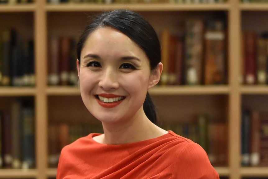 The writer Alice Pung standing in front a bookshelf