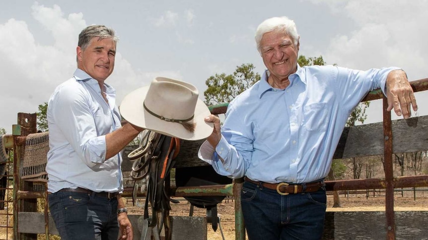 Bob and Robbie Katter wearing blue shirts holding a cowboy hat outside a cattle pen