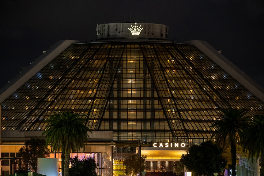 A large building with sloping glass walls backlit by lights illuminating windows and a white casino sign.