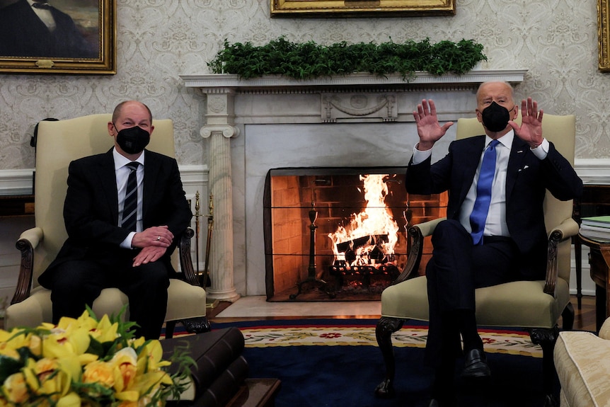 Joe Biden and Olaf Scholz sit on armchairs in front of a fireplace to address press. 