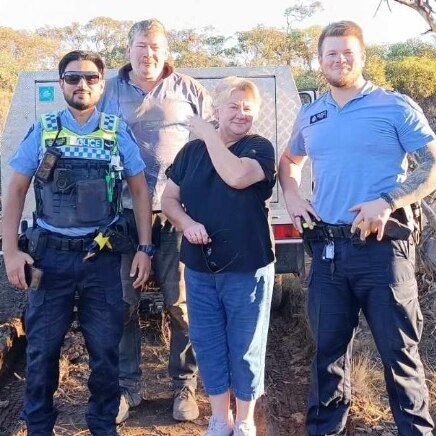 white car bogged in mud and four people - three men and one woman pose form a photo in scrubland