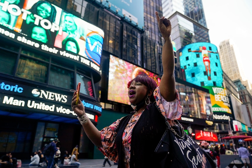 A woman raises her arm in celebration while walking through Times Square in New York