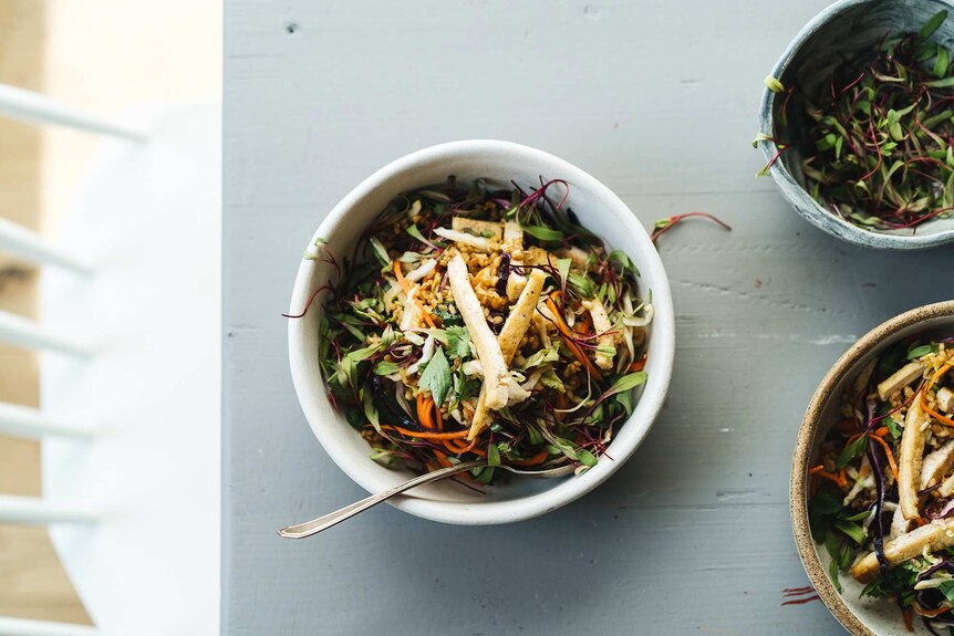 A bowl of crispy rice salad topped with tofu, herbs and vegetables sits on a dining table, for a shared meal.