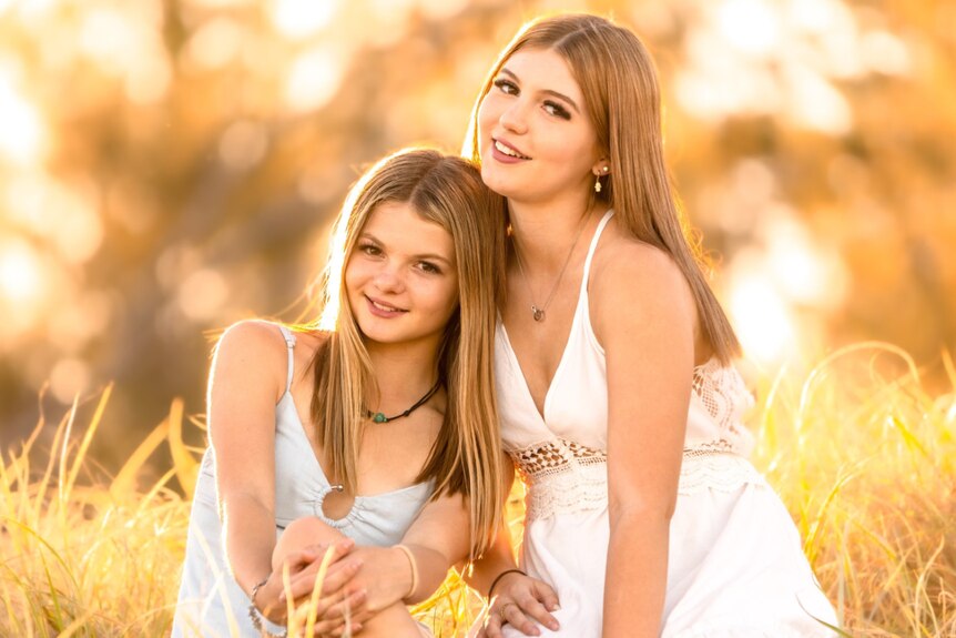 Two teen girls sitting on a sand dune with golden light behind them