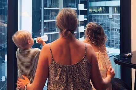 The back of a woman and her two children looking outside a window.