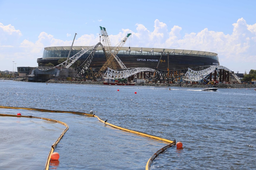 The Matagarup Bridge under construction alongside the Swan River with Perth Stadium behind it and water in the foreground.