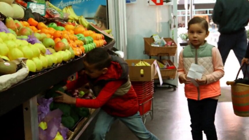 Children in a store standing next to the fruit section