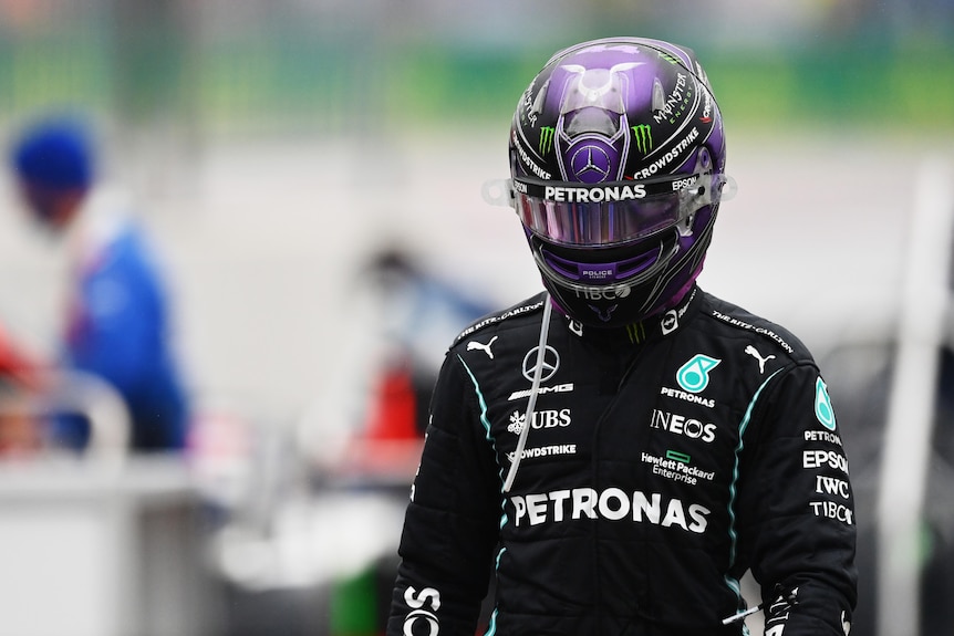 Race driver with purple helmet looks down.